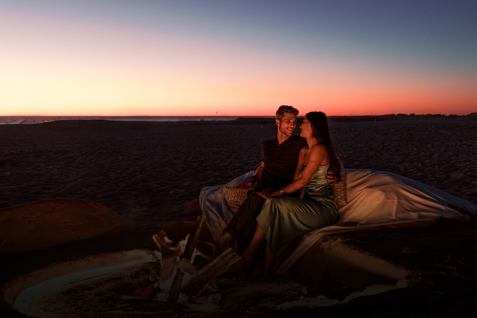 a man and woman sitting on a blanket on a beach